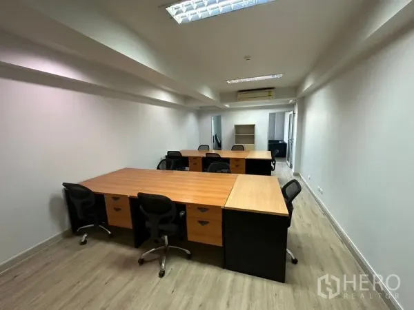 办公空间 出租在Khlong Toei, Bangkok - 开放式办公室，配多组木质工位与黑色办公椅，木纹地板、白色墙面、吊顶日光灯与壁挂空调。