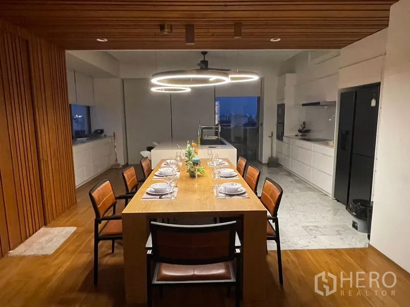 公寓 出租或出售在Watthana, Bangkok - 可供八人用餐的餐桌，旁为白色岛台厨房与环形吊灯