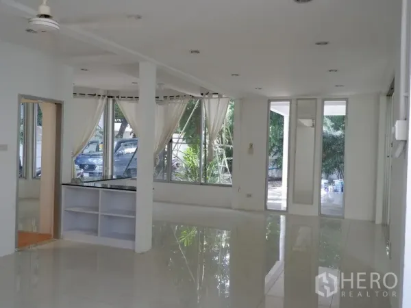 Detached House for rent in Khlong Toei, Bangkok - Bright open-plan living area with glossy floors, large windows and a ceiling fan.