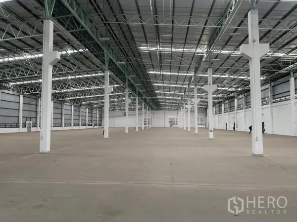 Factory for rent in Bang Sao Thong, Samut Prakan - Expansive warehouse interior with a high steel truss roof and rows of white columns.