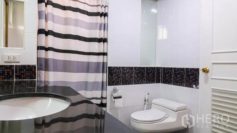 Condominium for rent or sale in Khlong Toei, Bangkok - Bathroom with striped shower curtain, vanity counter and toilet.