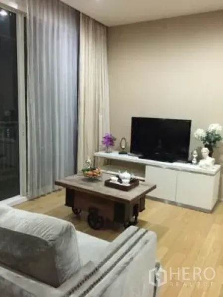 公寓 出租在Watthana, Bangkok - 现代客厅，灰色沙发、电视柜、木地板与落地窗帘的曼谷公寓。