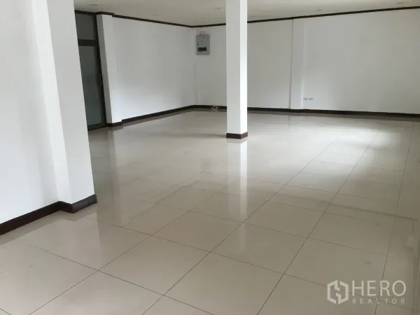 Townhouse for rent in Khlong Toei, Bangkok - Spacious open-plan living area with glossy ceramic tile floors, white walls, and structural columns.