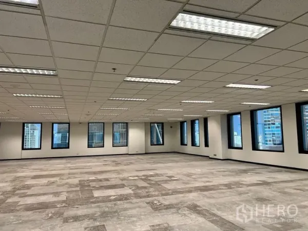 办公空间 出租在Khlong Toei, Bangkok - 大型办公室内部，局部铺设地砖，嵌入式日光灯，黑框窗外可见天际线。