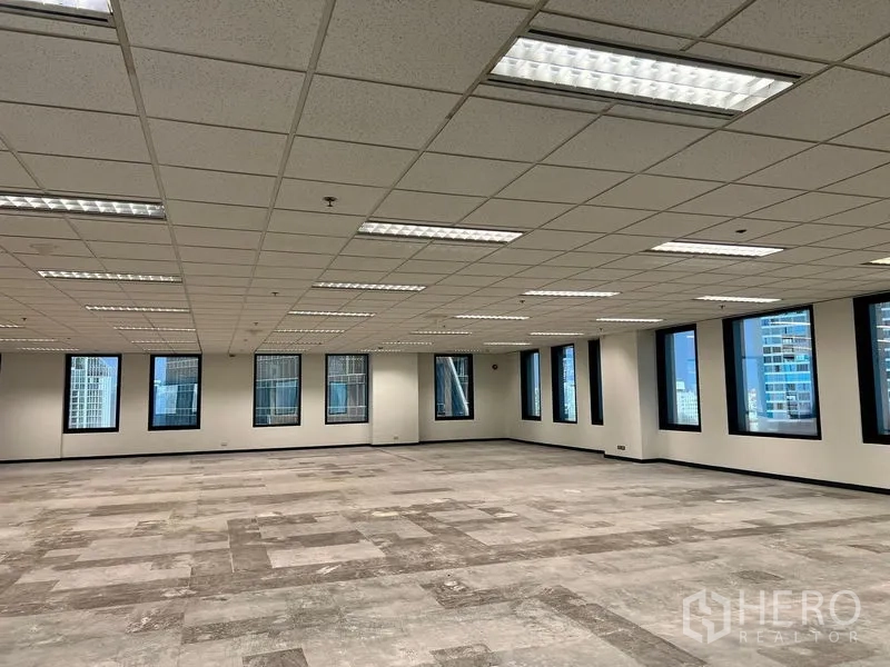 办公空间 出租在Khlong Toei, Bangkok - 大型办公室内部，局部铺设地砖，嵌入式日光灯，黑框窗外可见天际线。