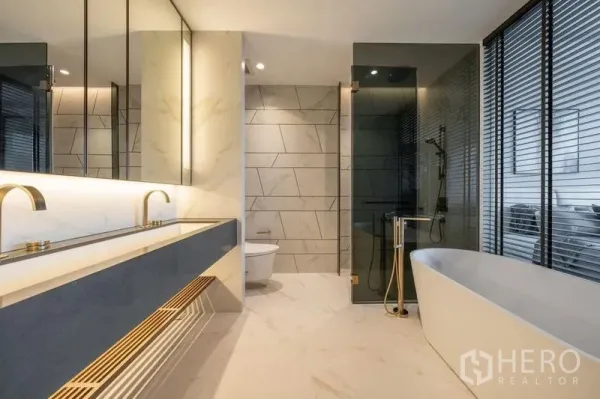 Condominium for rent in Khlong Toei, Bangkok - Modern bathroom with double vanity, freestanding bathtub and a glass-enclosed shower with brass fixtures.
