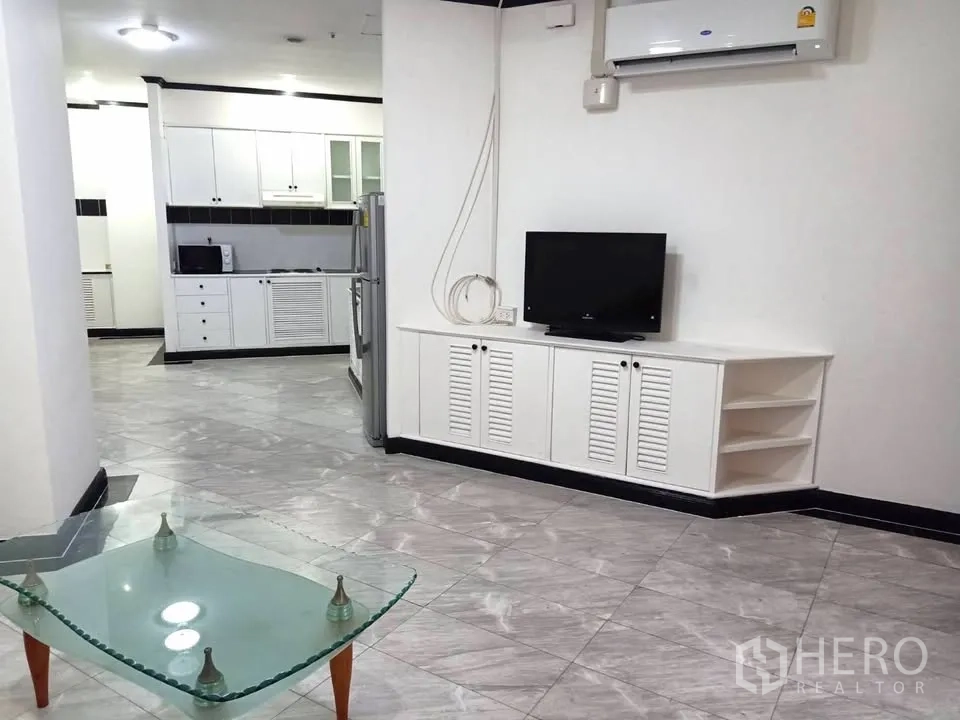 Condominium for rent in Watthana, Bangkok - Living area with TV console and glass coffee table facing the spacious kitchen.