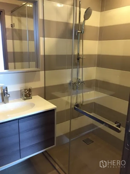 Condominium for rent in Watthana, Bangkok - Contemporary bathroom with striped wall tiles, glass shower enclosure, and floating vanity.