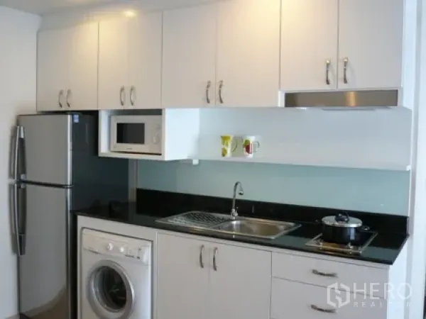 Condominium for rent in Watthana, Bangkok - Compact kitchen with white cabinetry, washing machine, microwave, and stovetop.