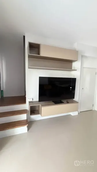 Townhouse for rent in Bang Phli, Samut Prakan - Living area with floating TV cabinet, wall shelves, and adjacent stairs.