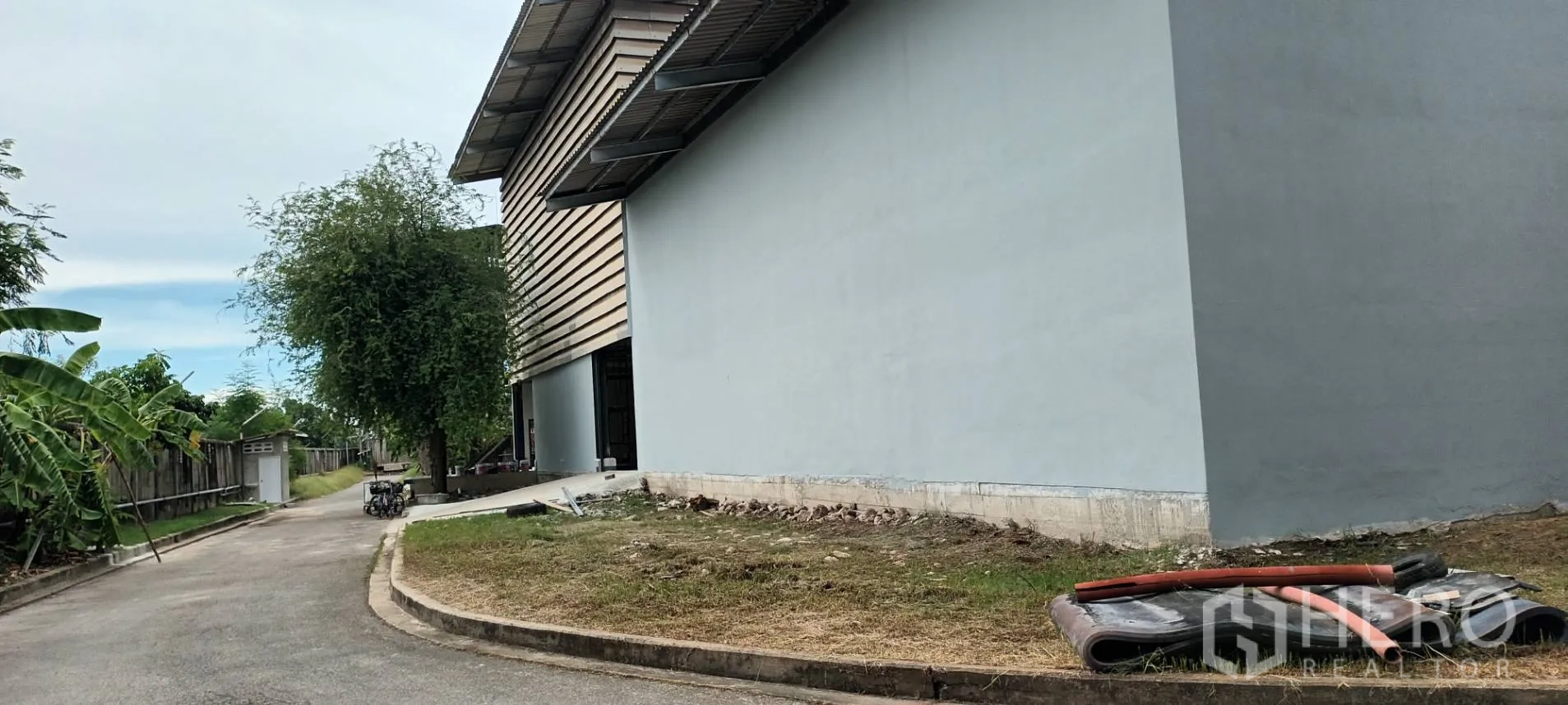 Warehouse for rent in Phra Pradaeng, Samut Prakan - Street-side view of the warehouse next to a boundary wall and mature trees.