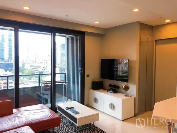 Condominium for rent in Bang Rak, Bangkok - Living room with balcony doors, TV console and city skyline view.