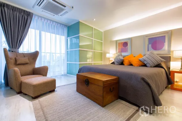 คอนโด ให้เช่าในPathum Wan, Bangkok - ห้องนอนมาสเตอร์พร้อมเตียงคิงส์ หมอนตกแต่ง เก้าอี้เอนพร้อมสเต็ป ตู้เสื้อผ้าบานเลื่อนกระจก และประตูออกสู่ระเบียง