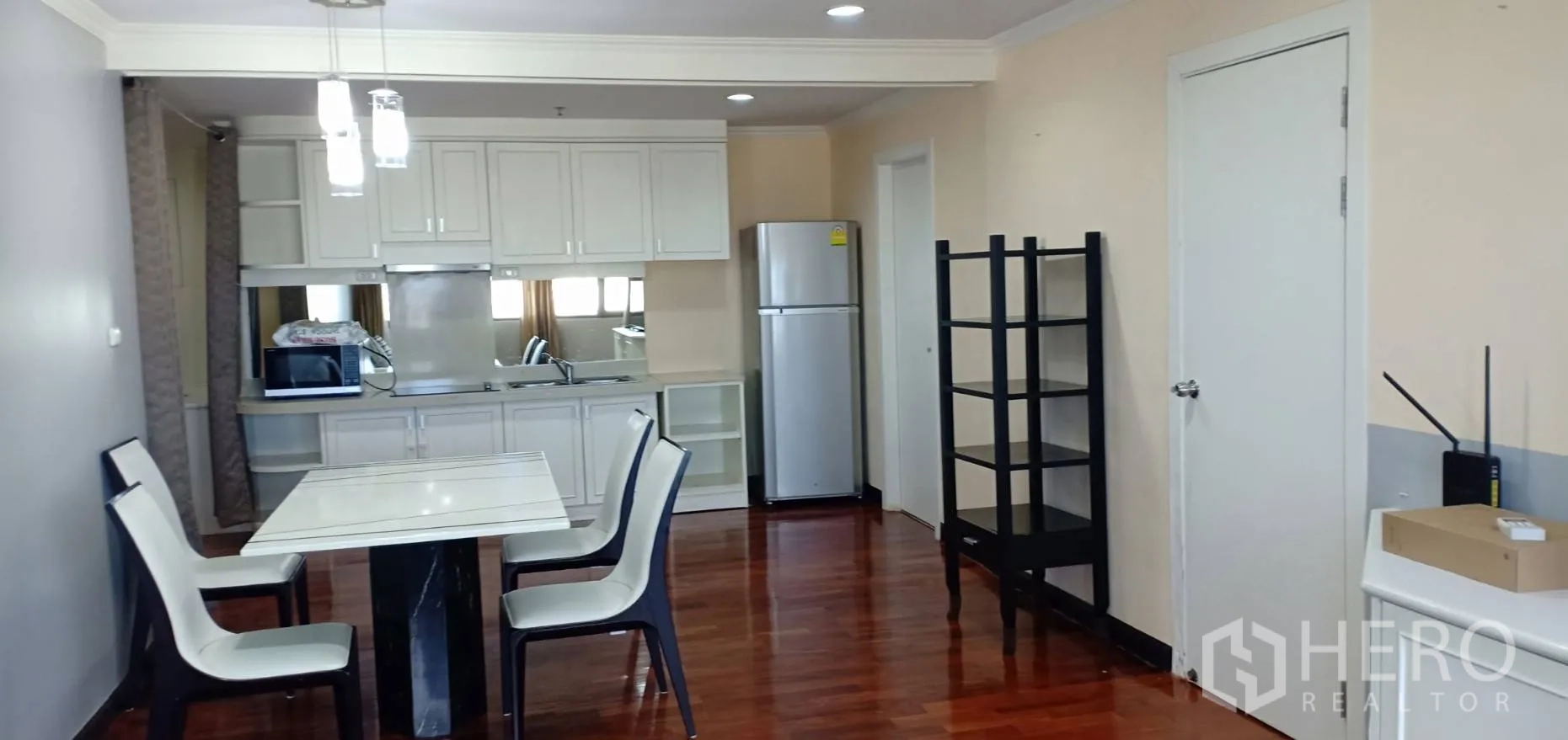 Condominium for rent in Watthana, Bangkok - Bright dining space beside a white fitted kitchen with pendant lights, refrigerator and shelving on polished wooden floors.