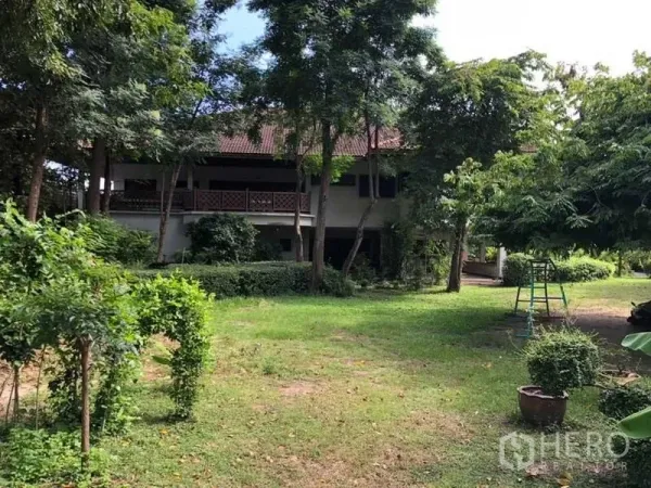 Detached House for sale in Bang Na, Bangkok - Lush garden with mature trees facing a two-storey detached house with balcony.