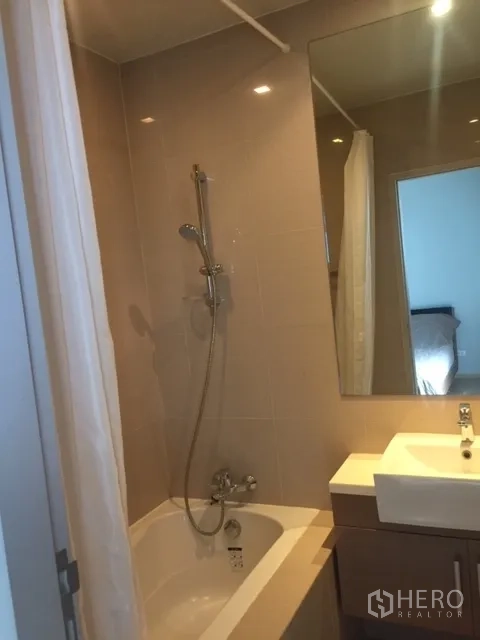 Condominium for rent in Bangkok - Bathroom with bathtub-shower combination, large mirror and modern vanity.