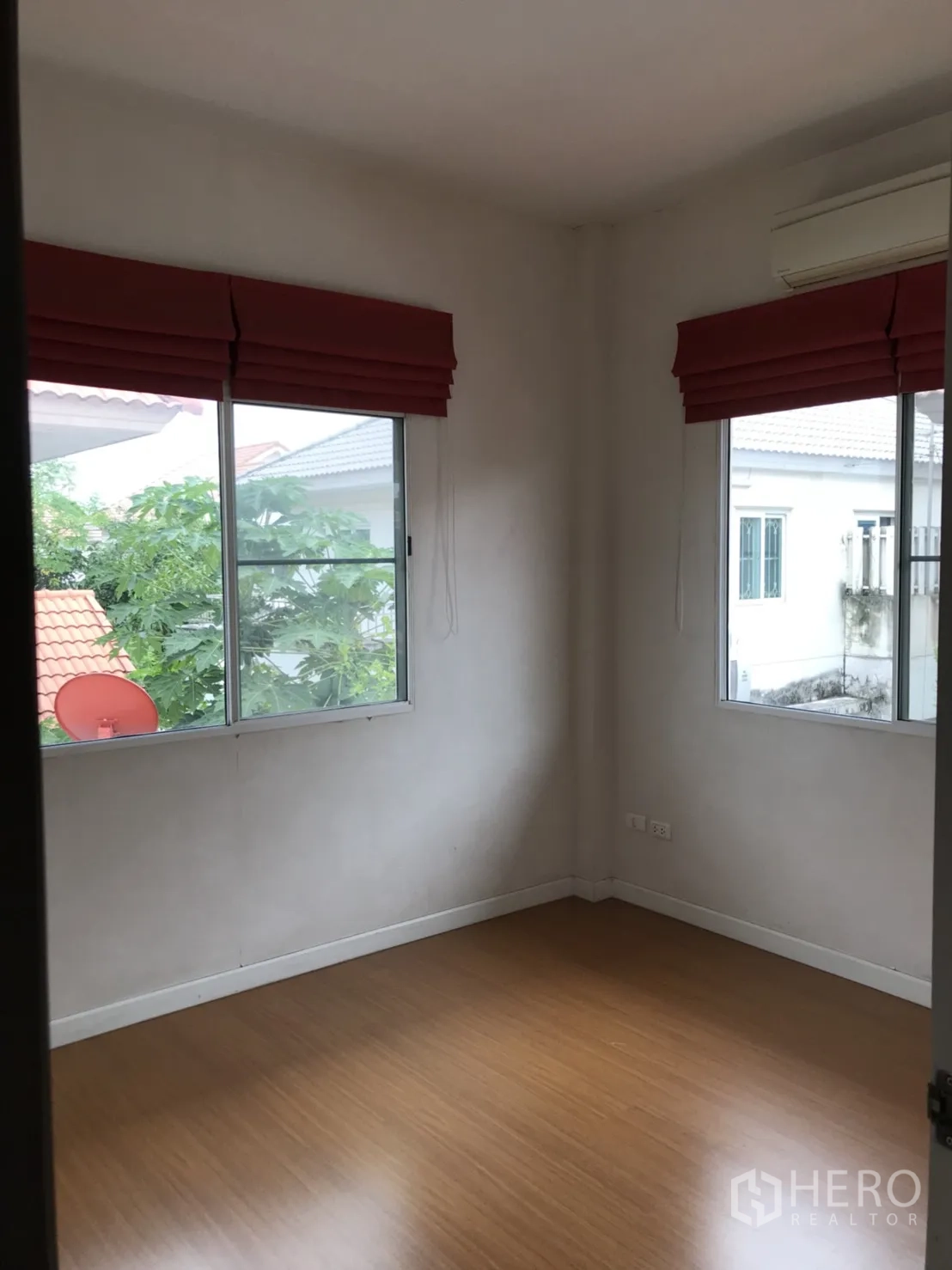 Detached House for rent in Lat Krabang, Bangkok - Corner bedroom with two windows, red roman blinds and wood-look flooring.