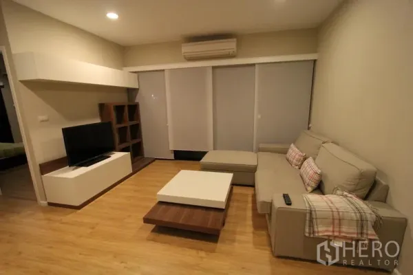 Condominium for rent in Pathum Wan, Bangkok - Cozy living room with L-shaped sofa, TV console, wooden flooring and sliding doors with blinds.