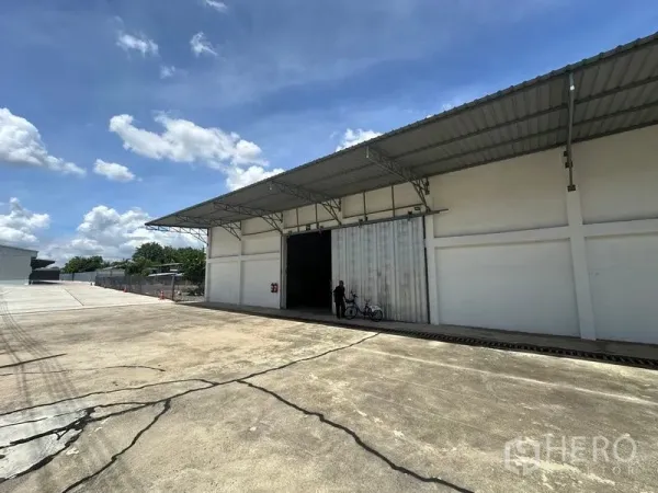 Warehouse for rent in Mueang Pathum Thani, Pathum Thani - Angled view of the warehouse showing spacious driveway, covered loading bay and oversized sliding entrance.