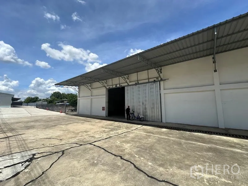 Warehouse for rent in Mueang Pathum Thani, Pathum Thani - Angled view of the warehouse showing spacious driveway, covered loading bay and oversized sliding entrance.