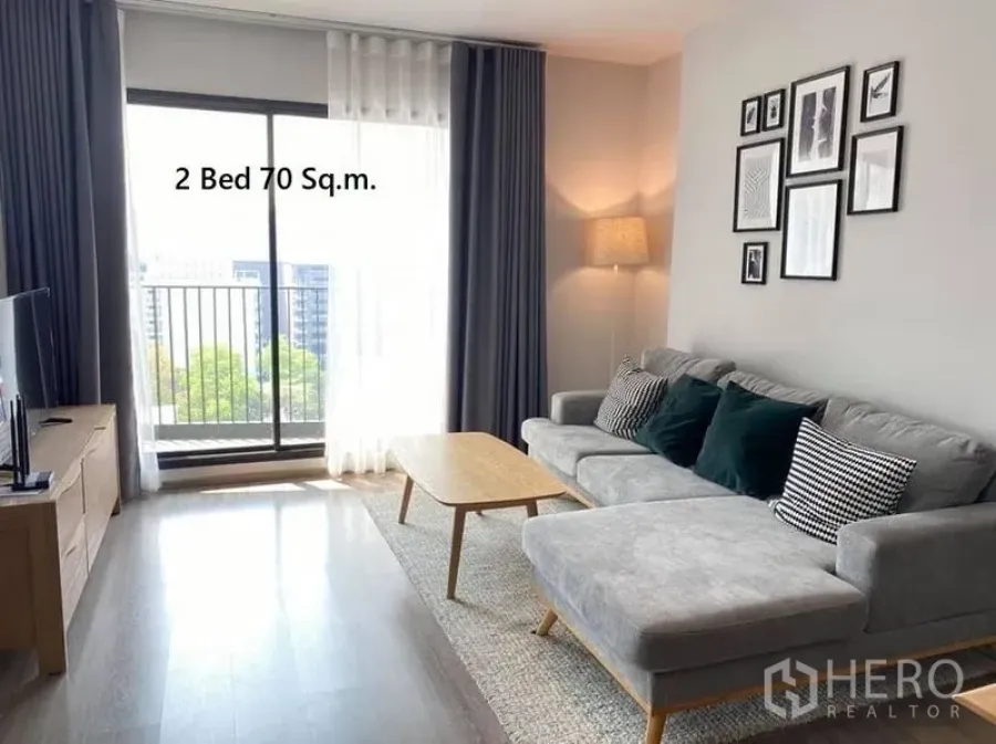公寓 出租在Watthana, Bangkok - 舒适起居区，转角沙发、电视柜，推拉门通往小阳台，享城市景观。