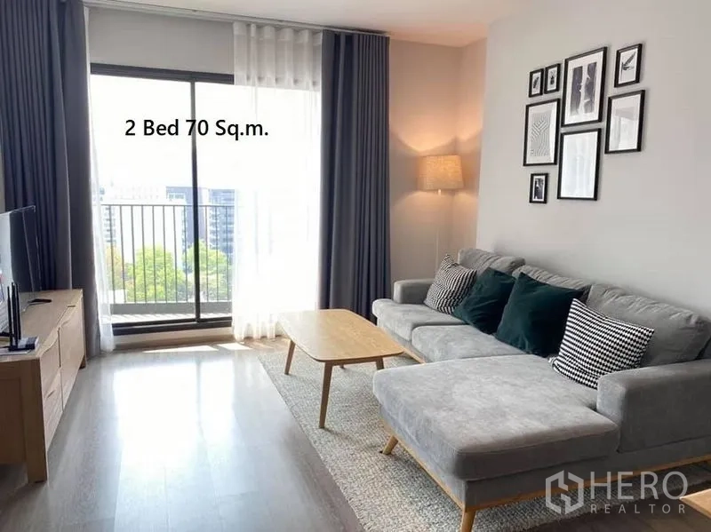 公寓 出租在Watthana, Bangkok - 舒适起居区，转角沙发、电视柜，推拉门通往小阳台，享城市景观。