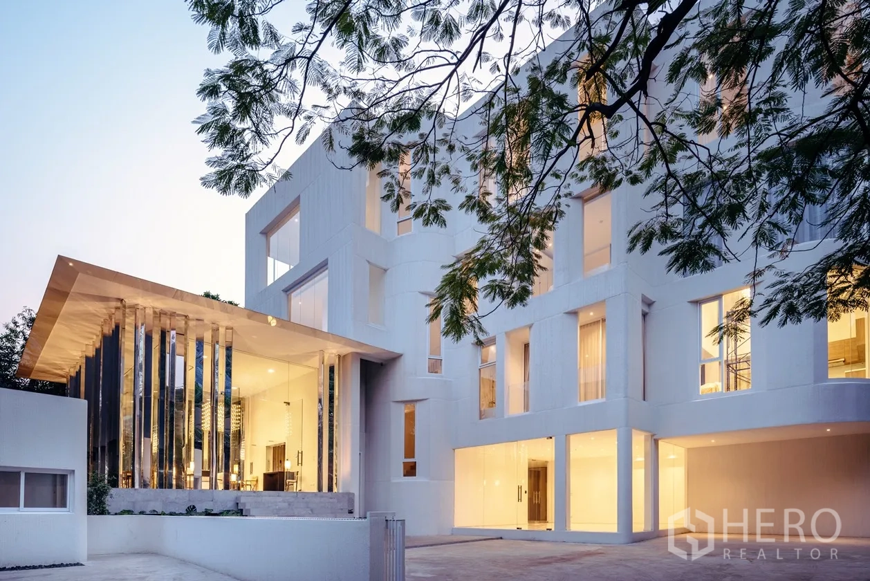 房间 出租在Khlong Toei, Bangkok - 现代低层公寓外观，带大型玻璃大堂，黄昏时分。
