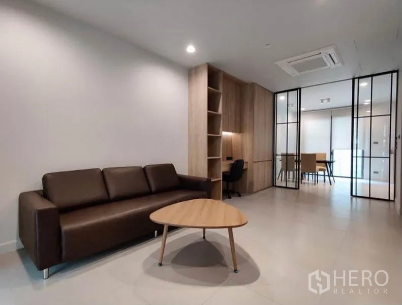 Townhouse for rent in Suan Luang, Bangkok - Open-plan lounge with brown sofa, built-in wood shelves and a study desk