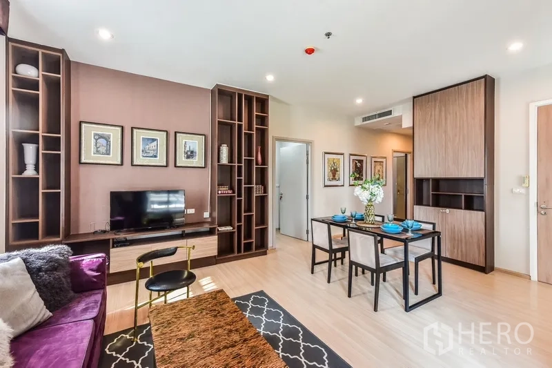 Condominium for rent or sale in Huai Khwang, Bangkok - Open lounge and dining space featuring custom wood shelving, TV unit, and modern lighting.