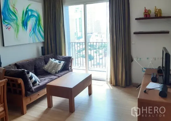 Condominium for rent in Khlong Toei, Bangkok - Bright living room with wooden sofa, coffee table and sliding doors to a balcony with city view.