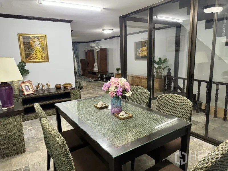 联排别墅 出租在Prawet, Bangkok - 次餐区/会客区，玻璃餐桌与藤编座椅，邻近玻璃隔断。