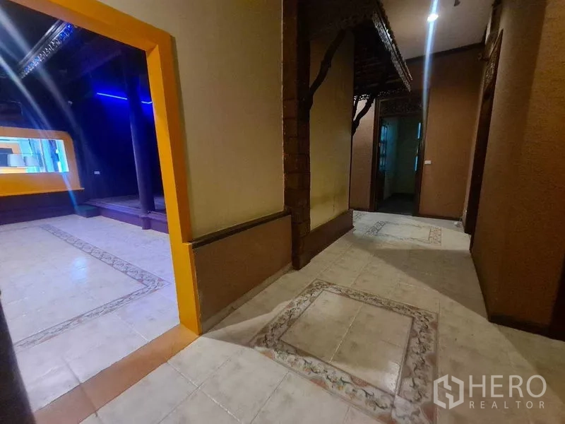 零售空间 出租在Watthana, Bangkok - 带花纹瓷砖的走廊，通向紫色零售区与抬高的展示台。