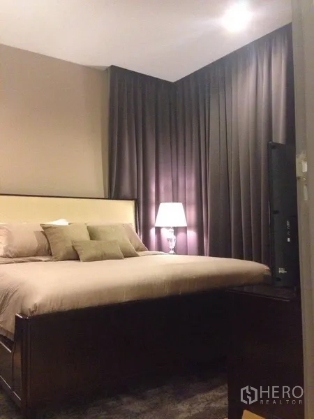 Condominium for rent in Khlong Toei, Bangkok - Master bedroom with king-size bed, bedside lamp and blackout curtains for privacy.