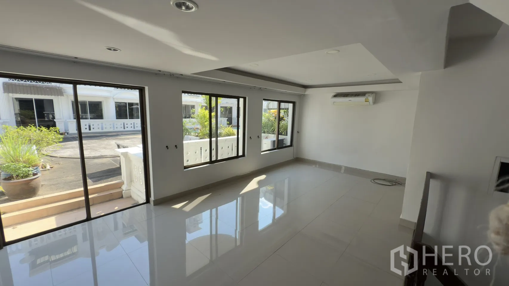 联排别墅 for rent in Watthana, Bangkok - 阳光客厅，数扇推拉窗通向带盆栽的阳台。