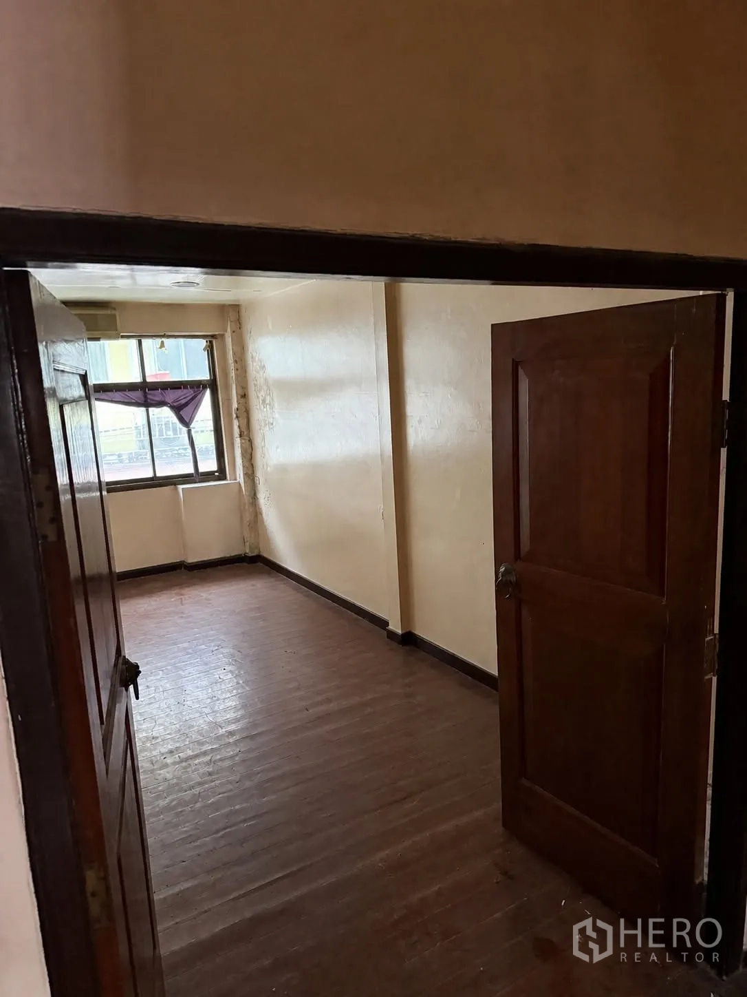 店屋 for rent in Bang Rak, Bangkok - 小房间铺木地板，奶油色墙面和窗户，从打开的木门内看到。