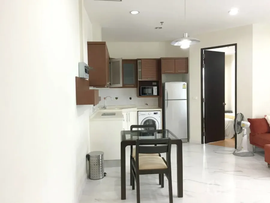 Condominium for rent in Khlong Toei, Bangkok - Open-plan living area with dining table and compact kitchen featuring fridge, microwave and in-unit washer.