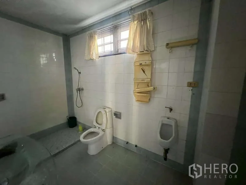 Detached House for rent in Prawet, Bangkok - Tiled bathroom with toilet, urinal and handheld shower under a window.