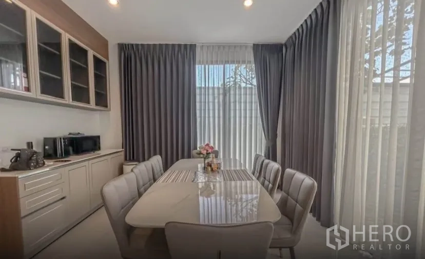Detached House for rent or sale in Lat Krabang, Bangkok - Bright dining area with six‑seat table next to tall curtained windows
