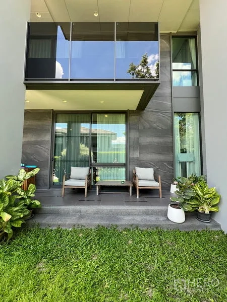 Detached House for rent in Bang Kapi, Bangkok - Covered back patio with two lounge chairs opening onto a small lawn and potted plants.