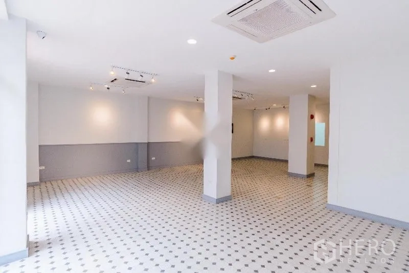 Home Office for rent in Khlong Toei, Bangkok - Spacious white interior with gallery-style lighting, tiled flooring and support columns suited for a showroom or office.