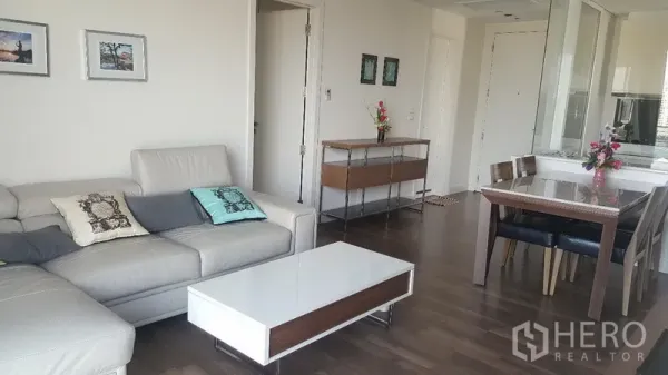 Condominium for rent in Bangkok - Living room with L-shaped leather sofa, white coffee table and wood flooring beside the dining area.
