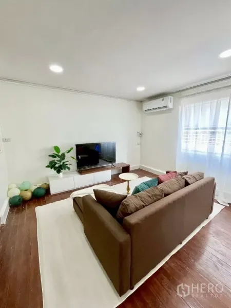 独立式住宅 出租在Chatuchak, Bangkok - 明亮客厅，棕色沙发、电视柜、木地板与纱帘。