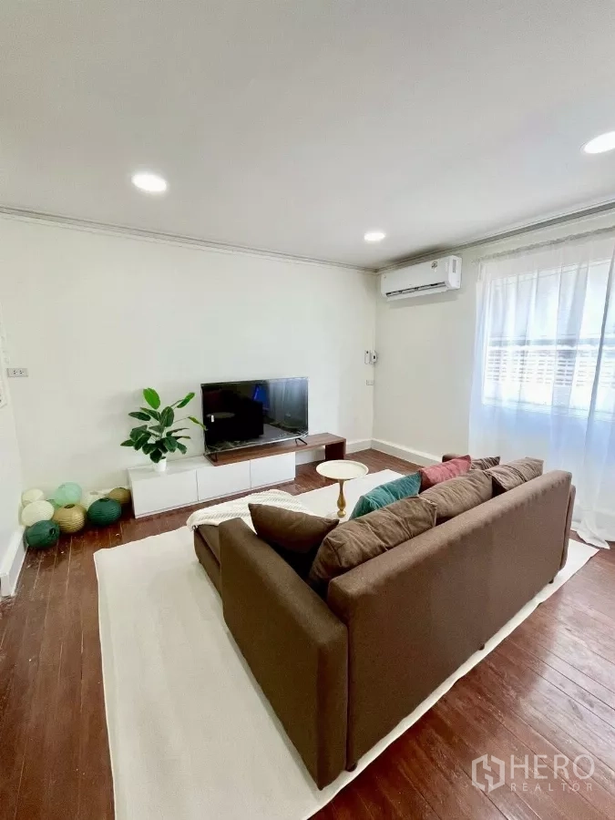 独立式住宅 出租在Chatuchak, Bangkok - 明亮客厅，棕色沙发、电视柜、木地板与纱帘。