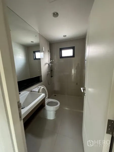 Detached House for rent or sale in Lam Luk Ka, Pathum Thani - Bathroom with large mirror, toilet and walk-in shower area with a small window.