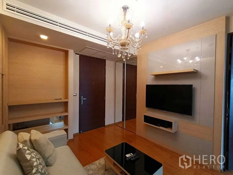 公寓 出租在Ratchathewi, Bangkok - 拉差贴威公寓客厅，水晶吊灯、木地板与定制电视墙，入口旁设沙发。