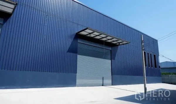 Warehouse for rent in Bueng Kum, Bangkok - Modern blue metal-clad warehouse exterior with large roller shutter, covered loading canopy and wide concrete driveway in Bueng Kum, Bangkok.