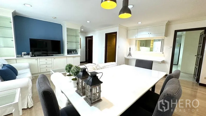 Condominium for rent or sale in Watthana, Bangkok - Dining table with gray chairs and pendant lights beside a TV storage wall.