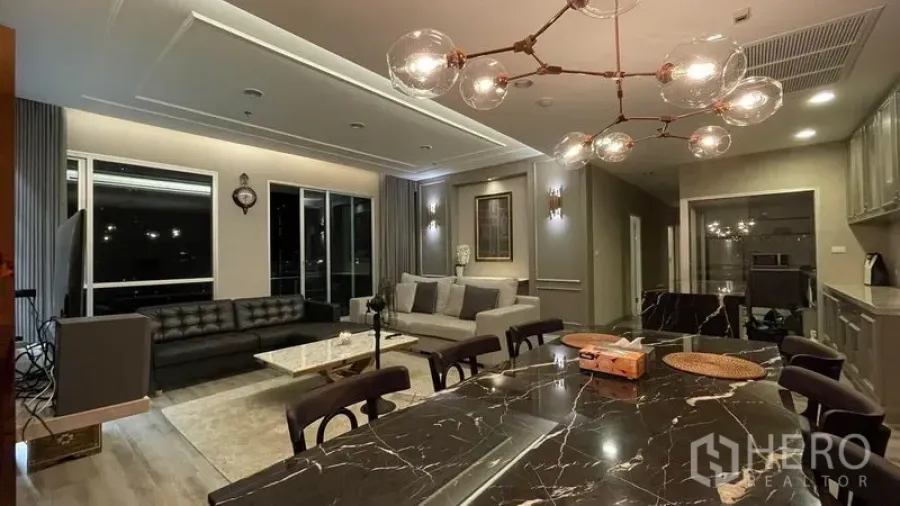 Condominium for sale in Sathon, Bangkok - Open-plan living and dining room with marble table, glass-bubble chandelier and large windows overlooking the city at night.
