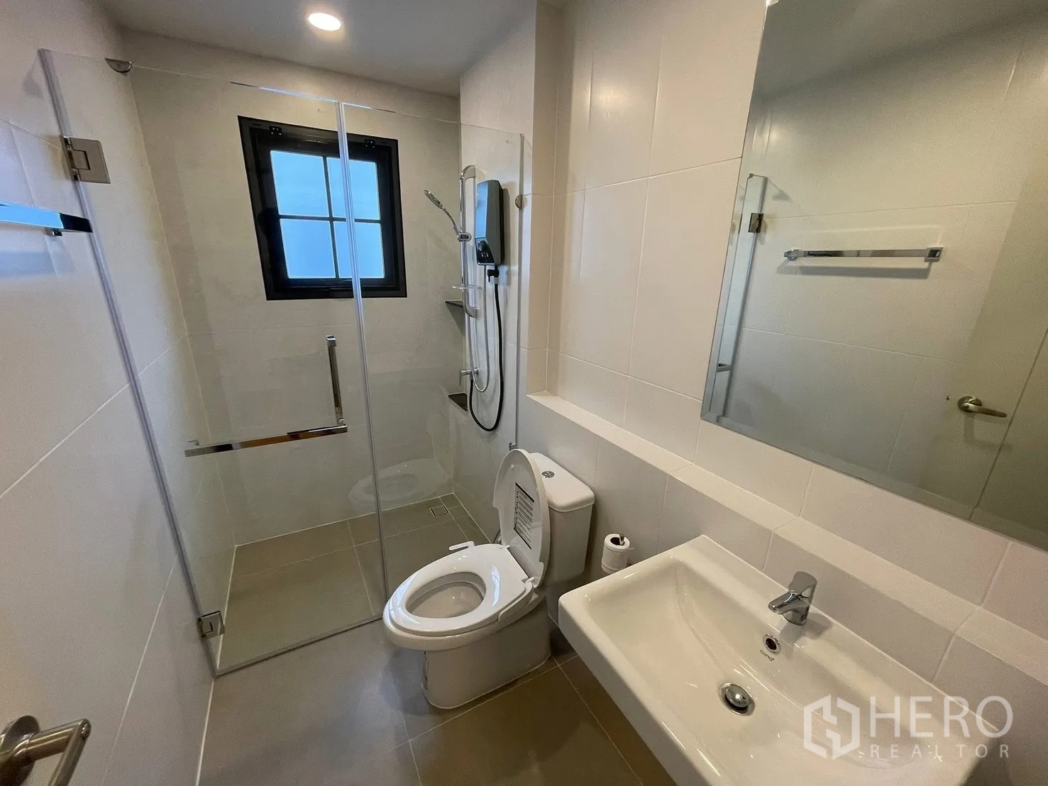 Detached House for rent in Bang Phli, Samut Prakan - Modern bathroom with glass-enclosed shower, white tile walls, vanity sink, and toilet under recessed lighting.