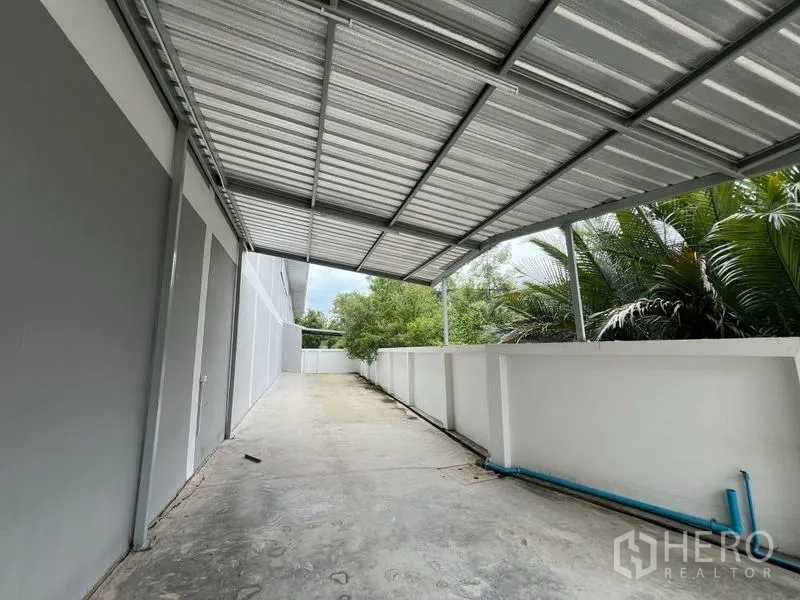 Factory for rent in Phra Samut Chedi, Samut Prakan - Covered side yard beside the factory with metal awning, concrete pathway and visible utility piping.